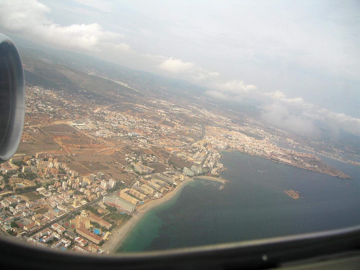 An aerial view of the Ibiza coastline, showing sandy coves and clear turquoise water.