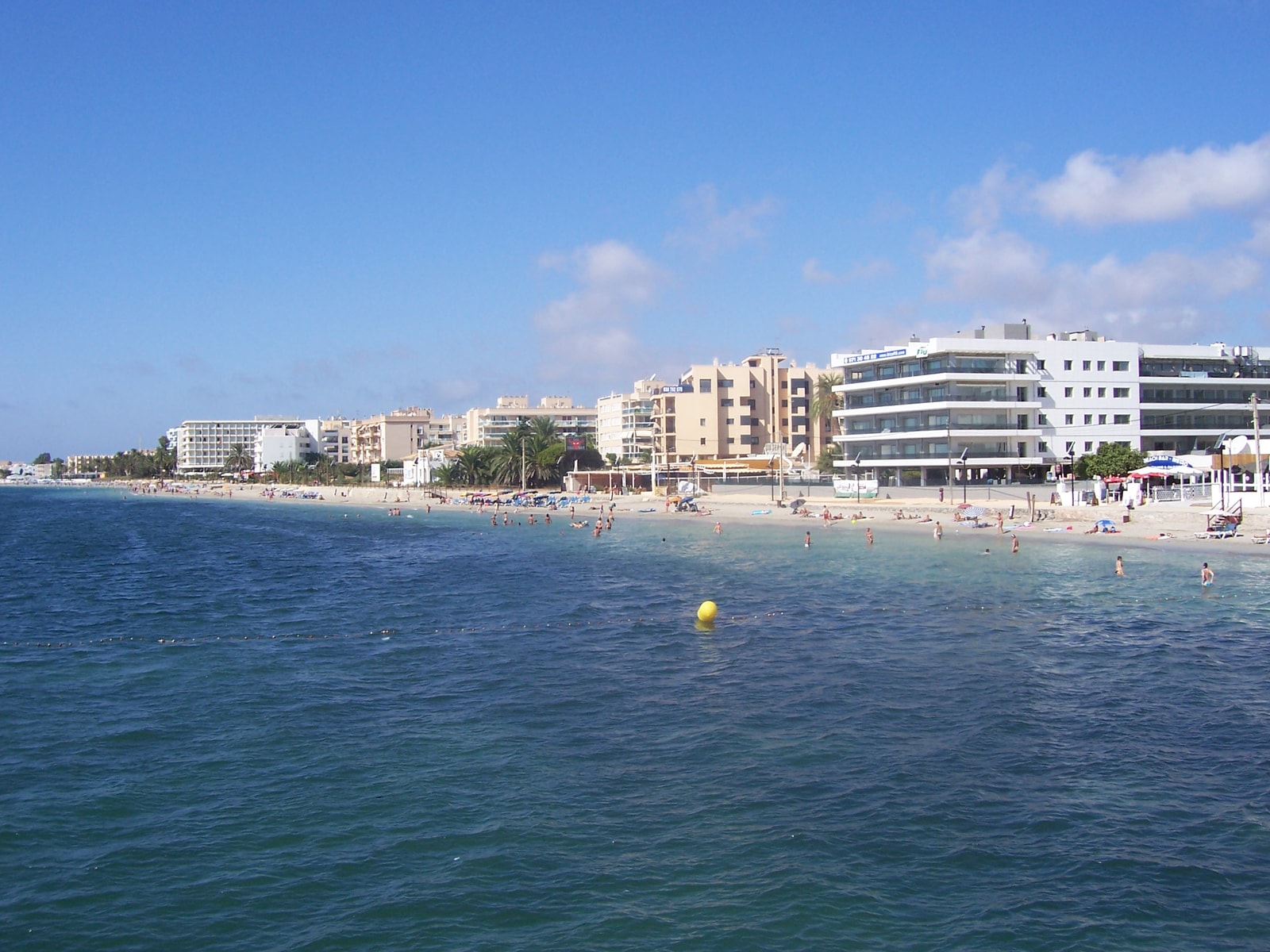 A view of the bustling Playa d'en Bossa beach, with its long stretch of sand lined with hotels, resorts, and sunbeds under a clear blue sky.