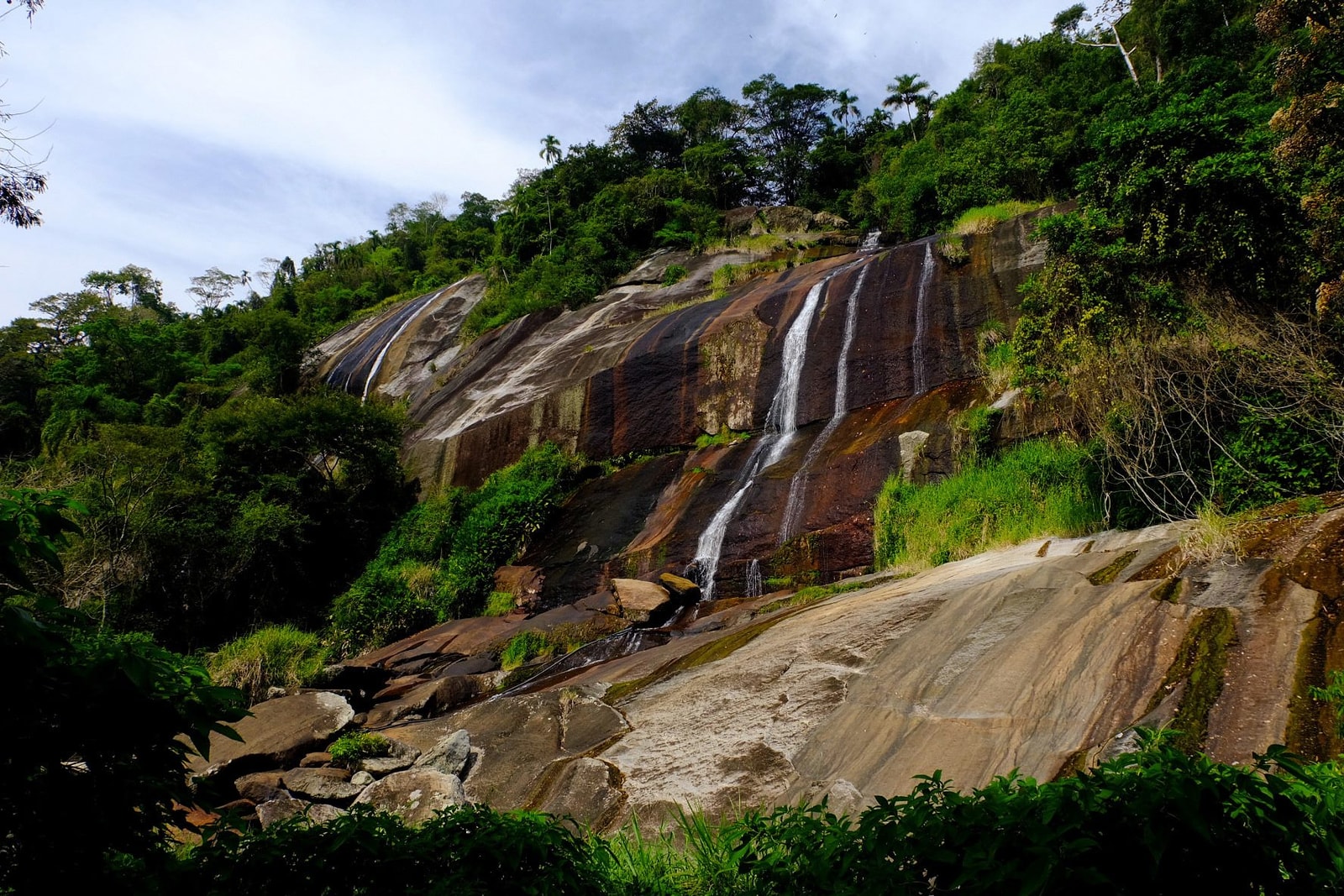 A rugged granite waterfall named Cachoeira da Água Branca flows through dense tropical vegetation in Ilhabela.