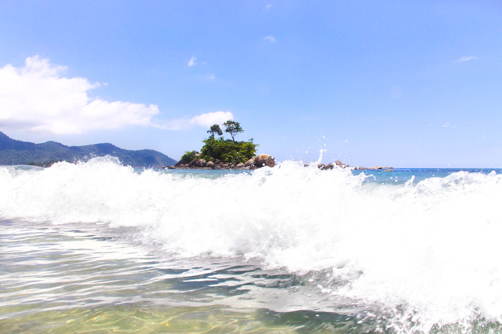 Waves crash on Castelhanos beach in Ilhabela, with a small island visible just offshore.