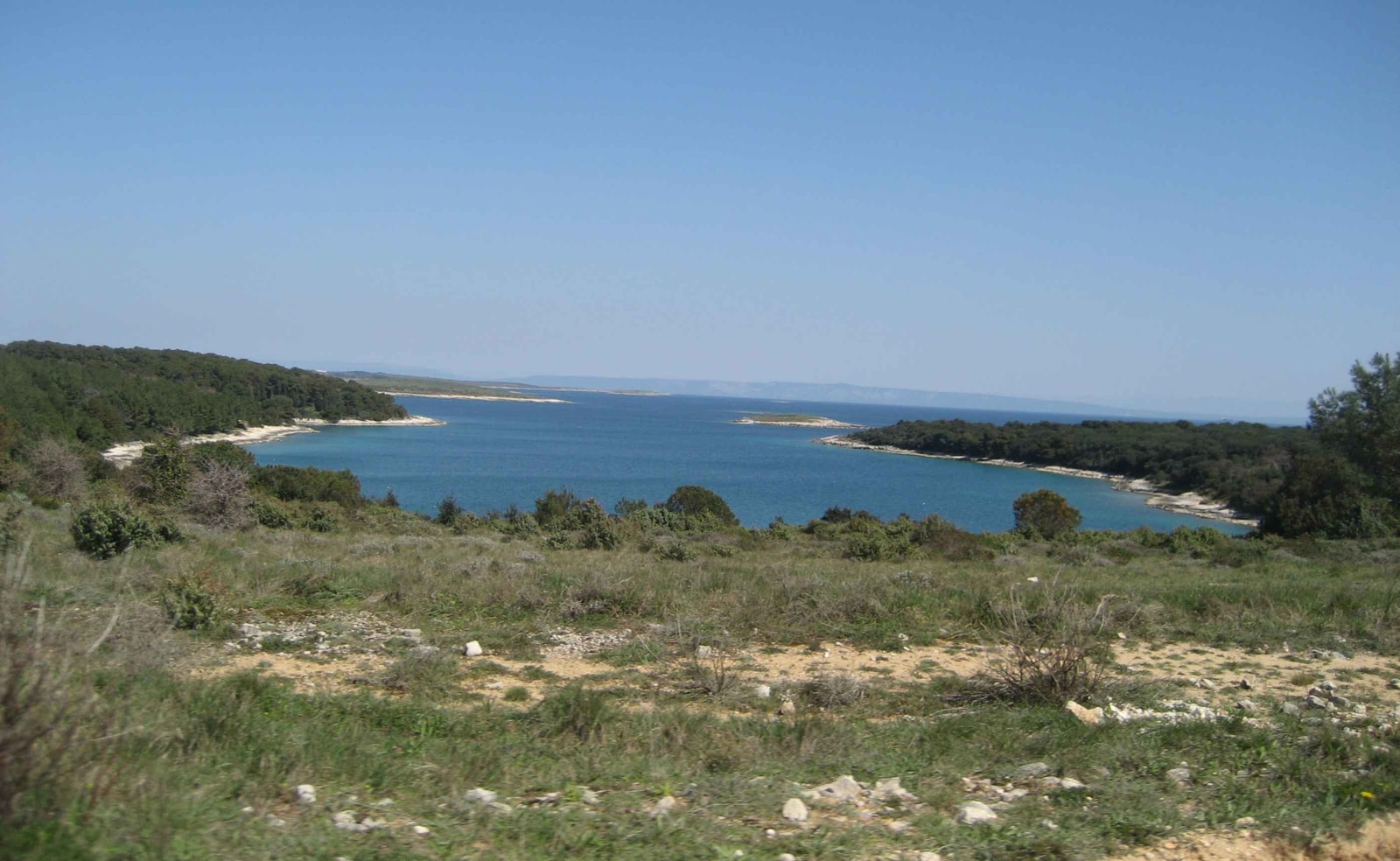 A deep blue inlet is surrounded by the rugged, rocky coastline and green scrub of the Cape Kamenjak nature reserve.