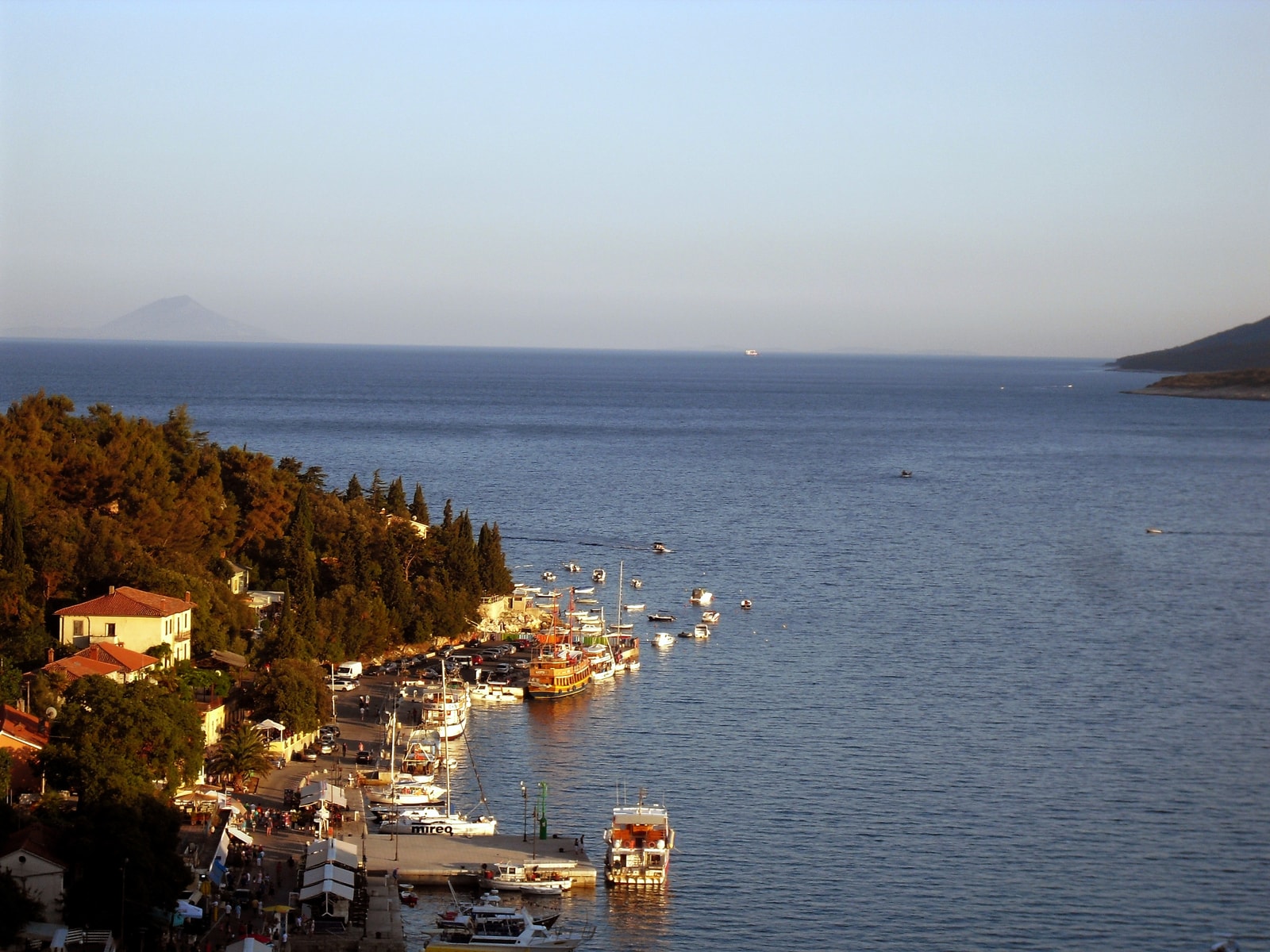 A panoramic, high-angle view of the town of Rabac, nestled in a wide bay with a harbor full of boats and surrounded by green hills.