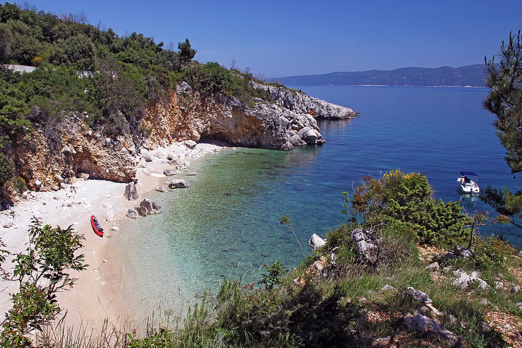 A secluded, small cove near Rabac with stunning emerald and turquoise water, framed by lush green vegetation and rocky cliffs.