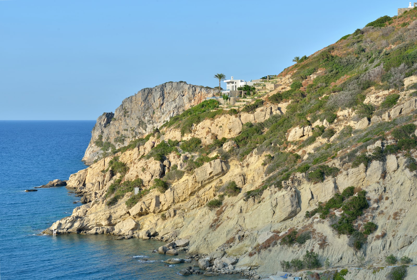 A view of the dramatic, rocky coastline of Istron Bay with deep blue water and coastal development on the hills.