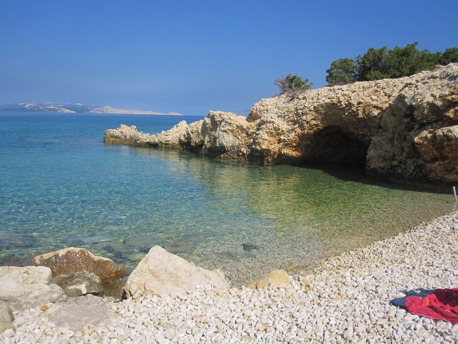 A secluded rocky cove near Stara Novalja with clear, shallow water and a small cave in the cliff.