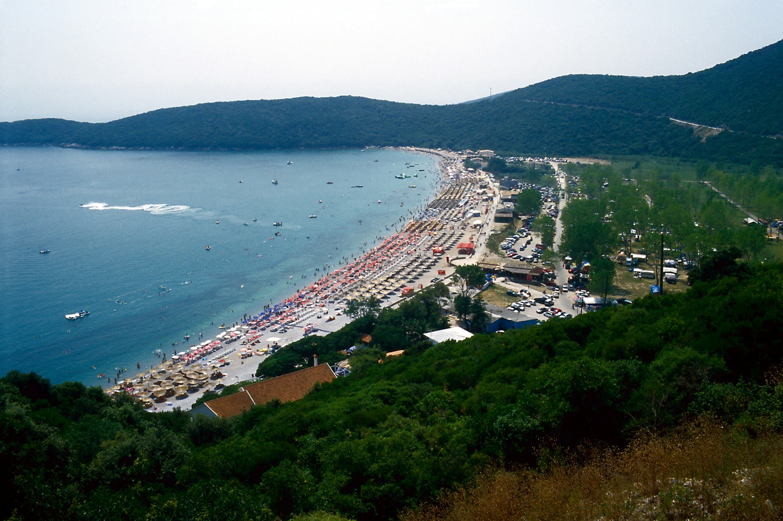 A high-angle view of a large bay with a long crescent beach, surrounded by green hills.