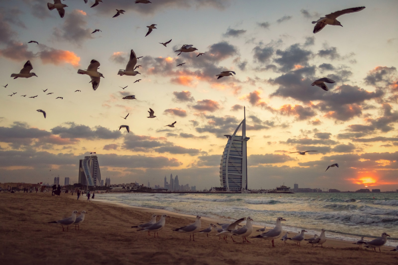 A dramatic sunset over Jumeirah Beach, with the silhouette of the Burj Al Arab against a golden sky and waves gently washing ashore.