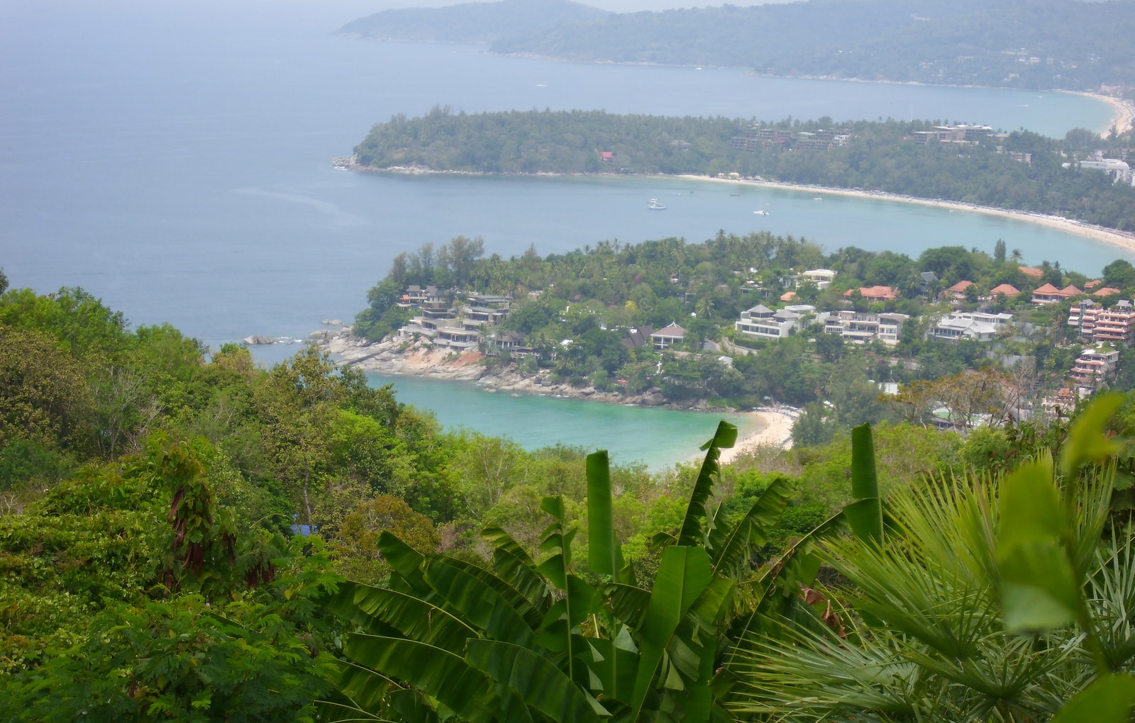 An elevated view from Karon Viewpoint looks over lush greenery towards several curving bays with turquoise water.