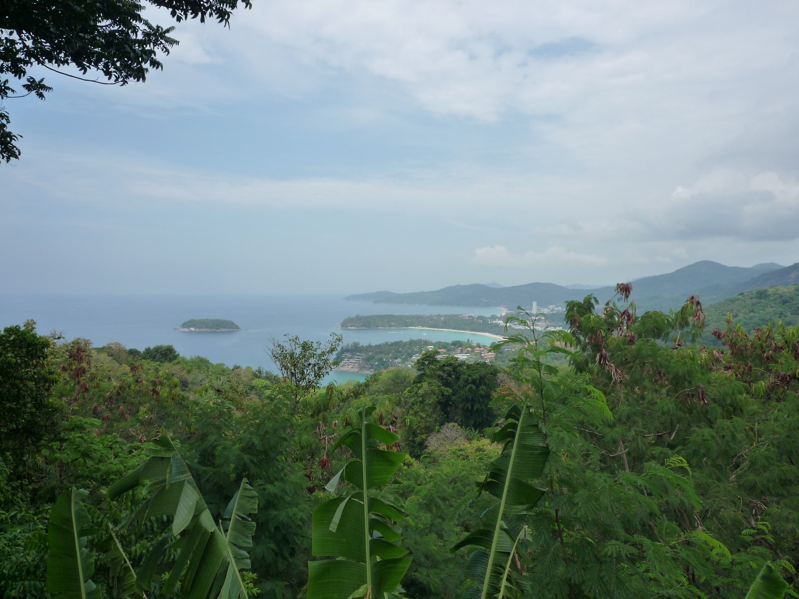 An elevated coastal view shows the layers of Phuket's landscape, with green hills, sandy bays, and offshore islands.