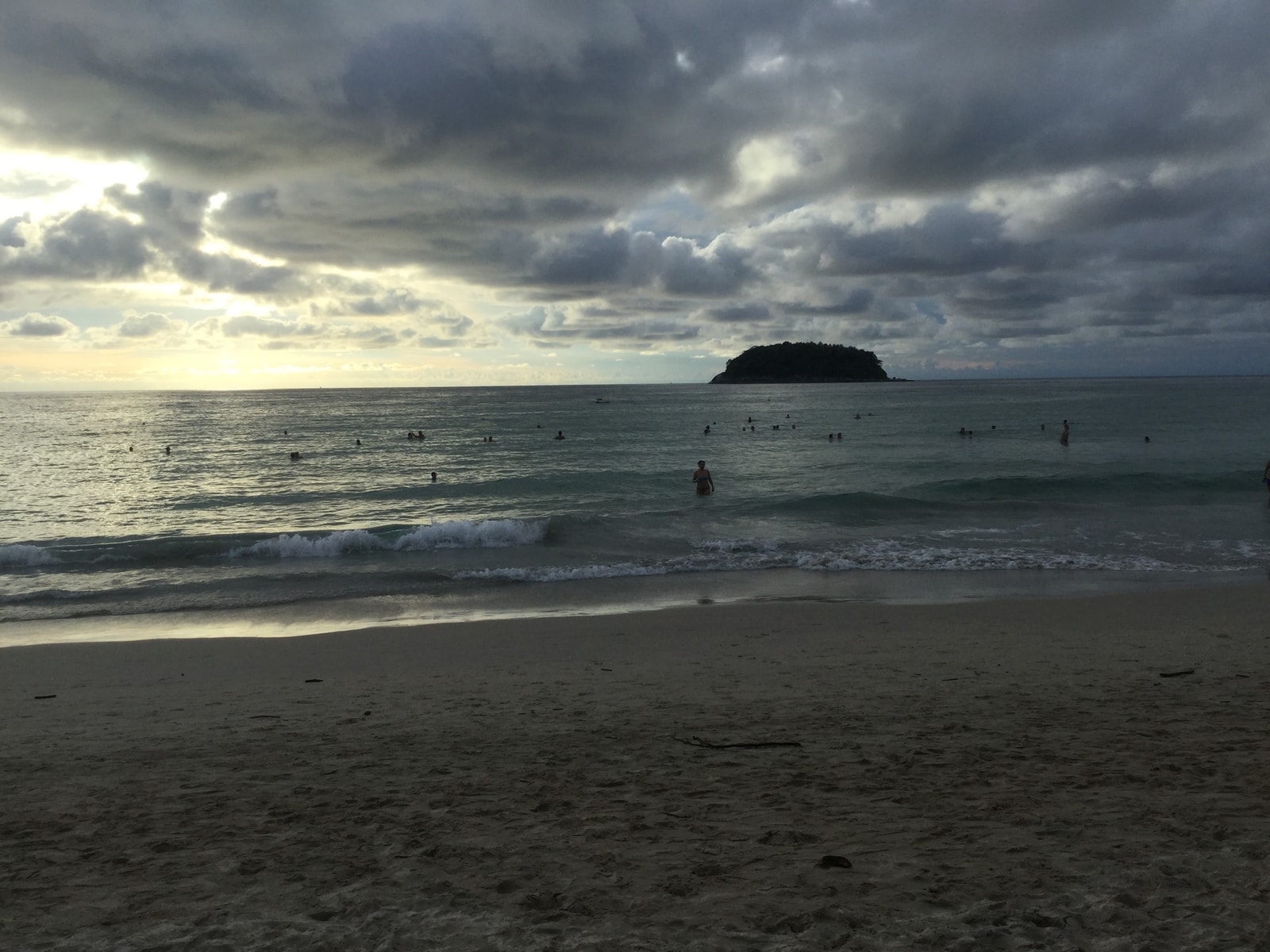 A setting sun casts a warm golden glow over Kata Beach, with the silhouette of Ko Pu island in the distance.