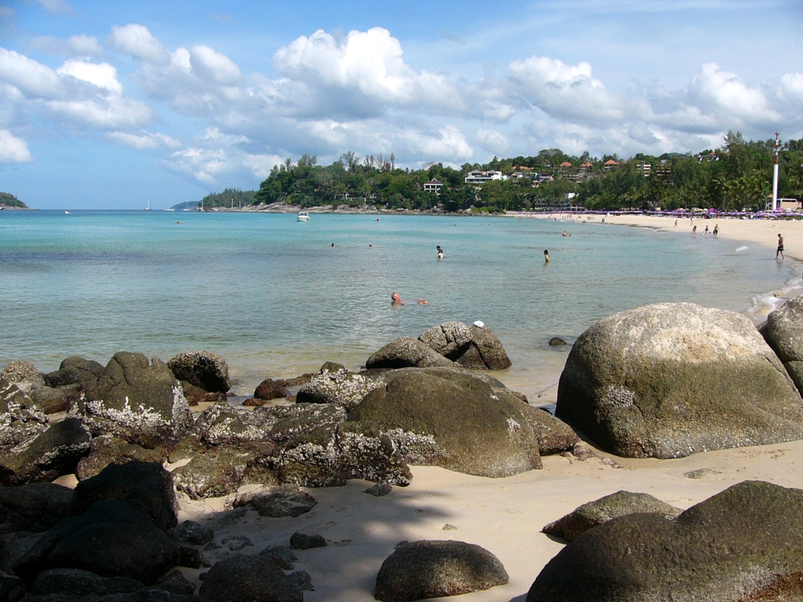 A rocky shoreline at Kata Noi beach, with clear water and a green hillside in the background.