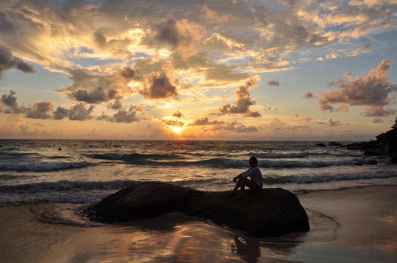 A moody sunset at Kata Noi beach, with the sun low on the horizon and its light reflecting on the wet sand.