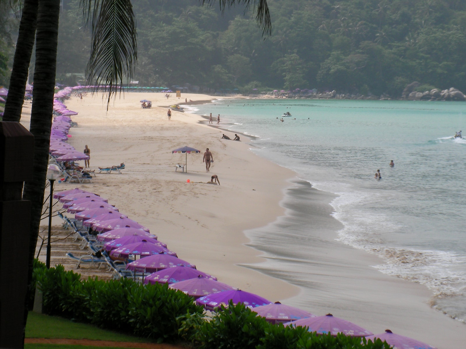 A view of a resort-backed beach, with rows of colorful umbrellas and sun loungers on the sand.