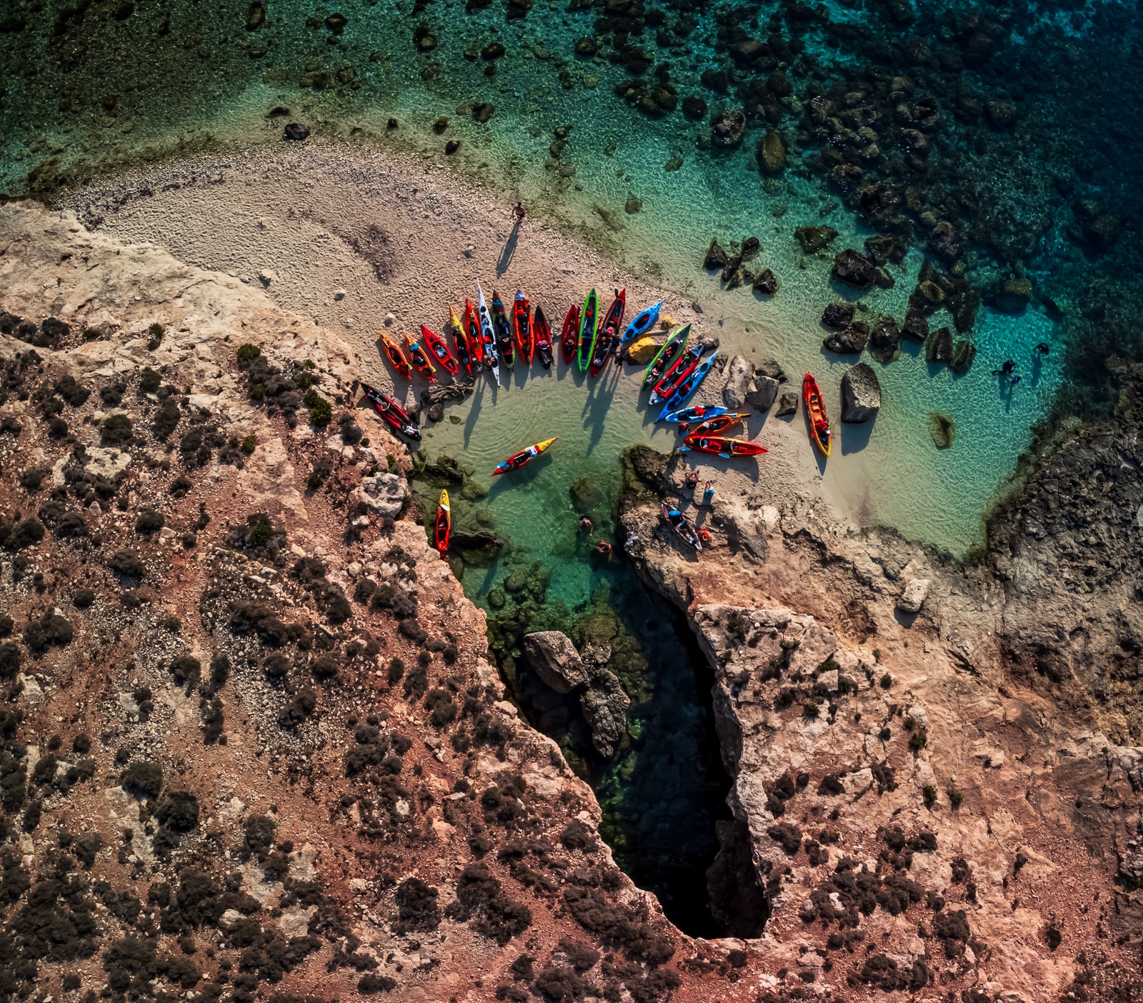 An overhead view of colorful kayaks resting on a small, rocky beach on Comino.