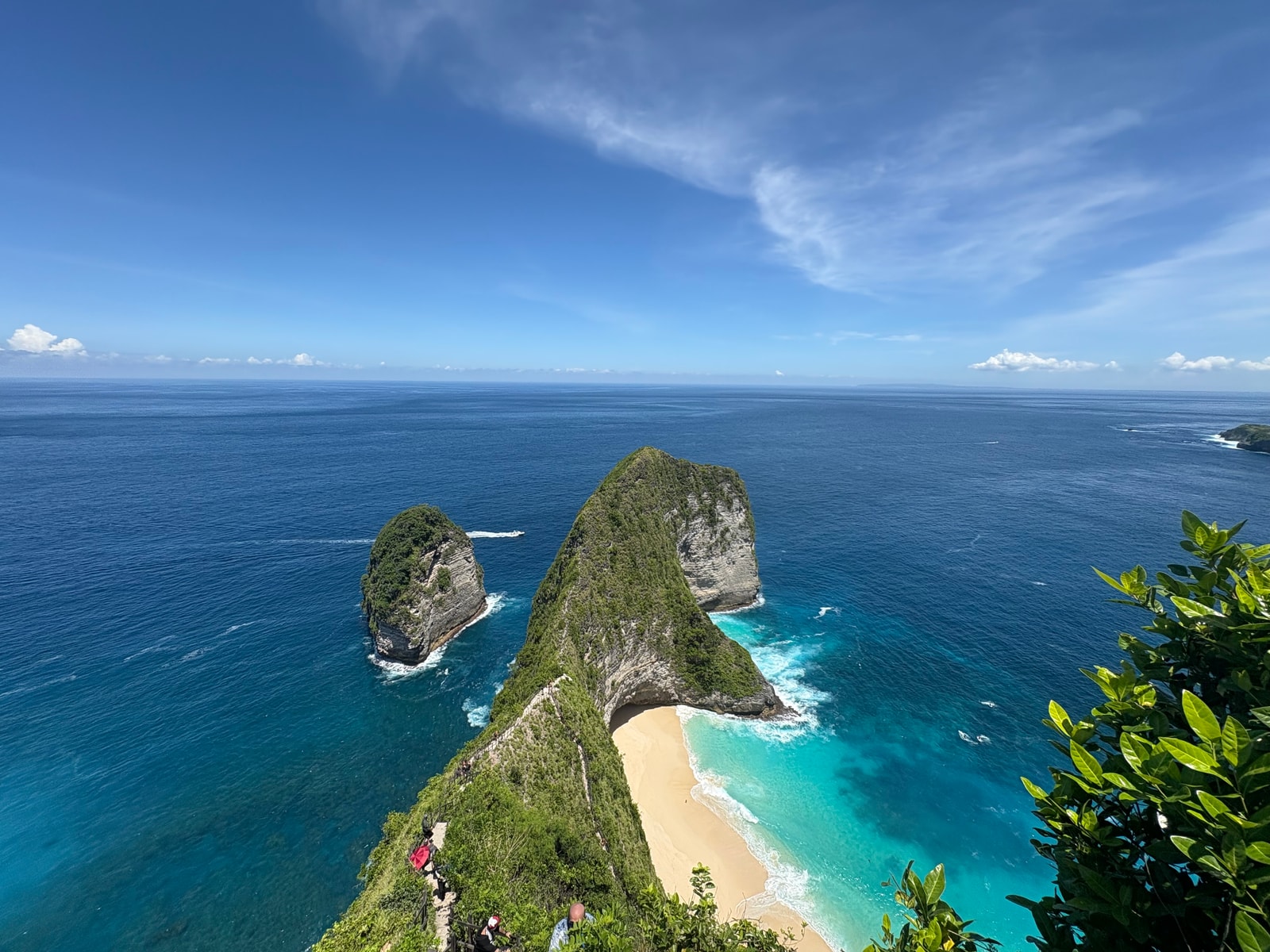 A elevated landscape view of Kelingking Beach shows the headland, beach, ridge, surf, and ocean.