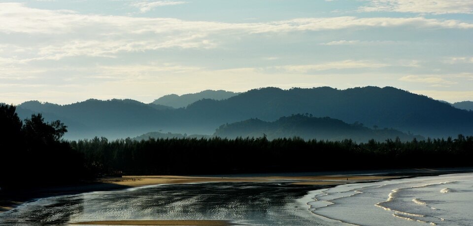 An atmospheric dawn scene at Pakarang Cape, with reflective tidal channels on the sand and misty hills in the distance.