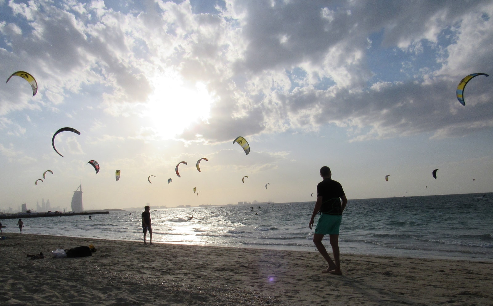 Numerous colorful kites fill the sky as people kitesurf in the ocean at dusk.