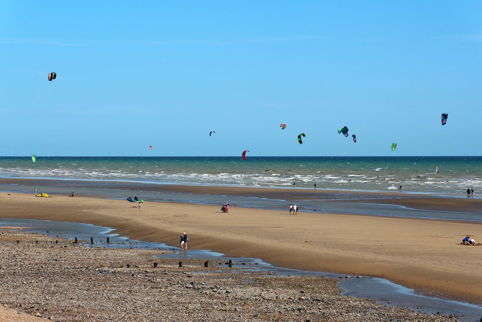 Multiple colorful kites fill the sky as kitesurfers ride in the shallow waters at Broomhill Sands.