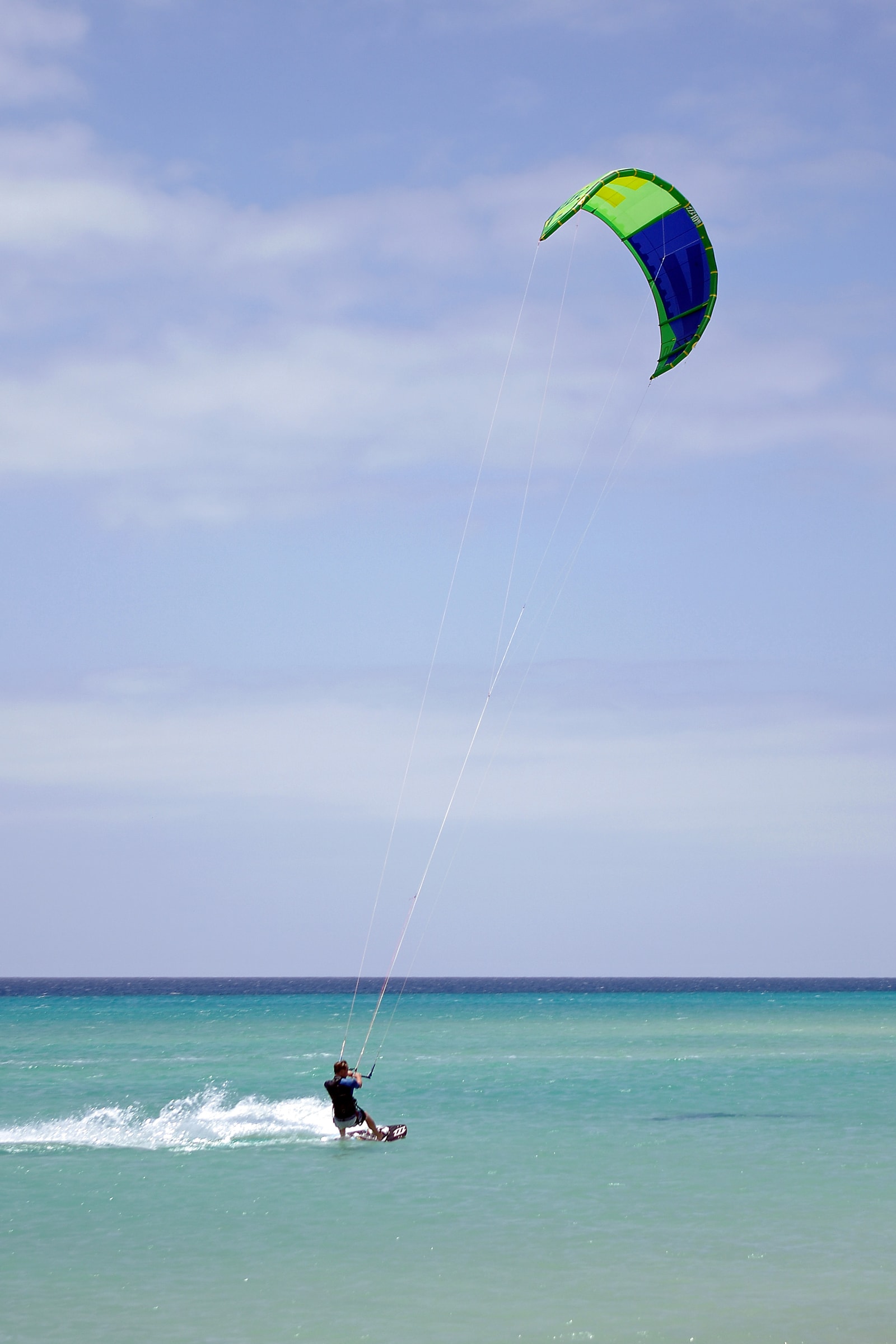 A kitesurfer's bright green and blue kite soars above the calm sea at Playa de Sotavento.