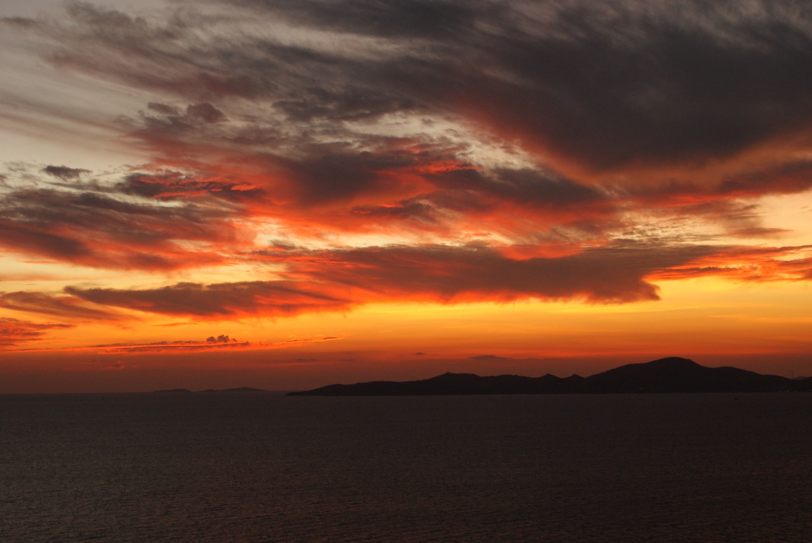 A dramatic sunset view over the sea from a high vantage point, with the silhouette of Ko Lan island on the horizon.
