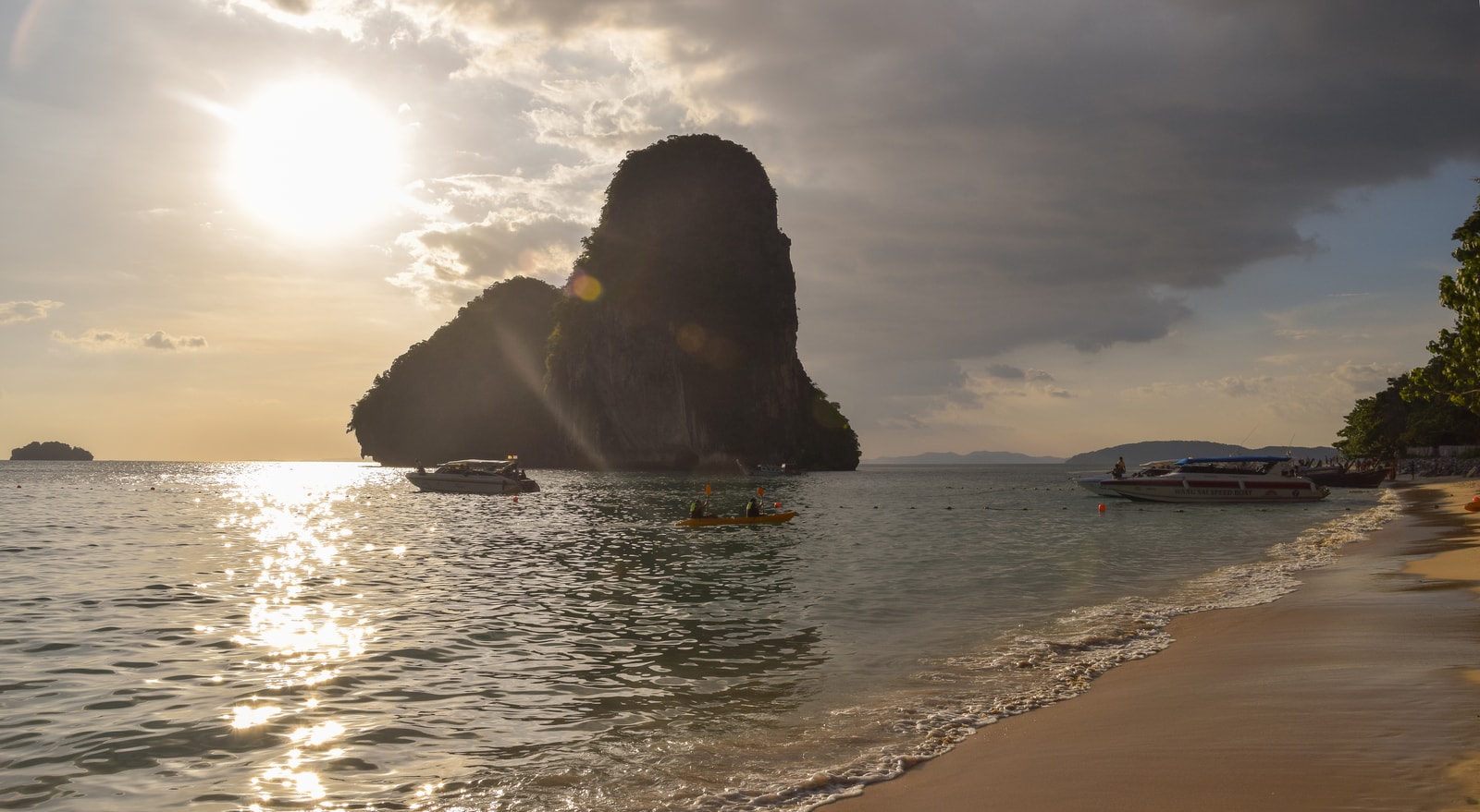 An overhanging rock ledge creates a dramatic frame for the view of a limestone karst island rising from the turquoise sea at Phra Nang Beach.