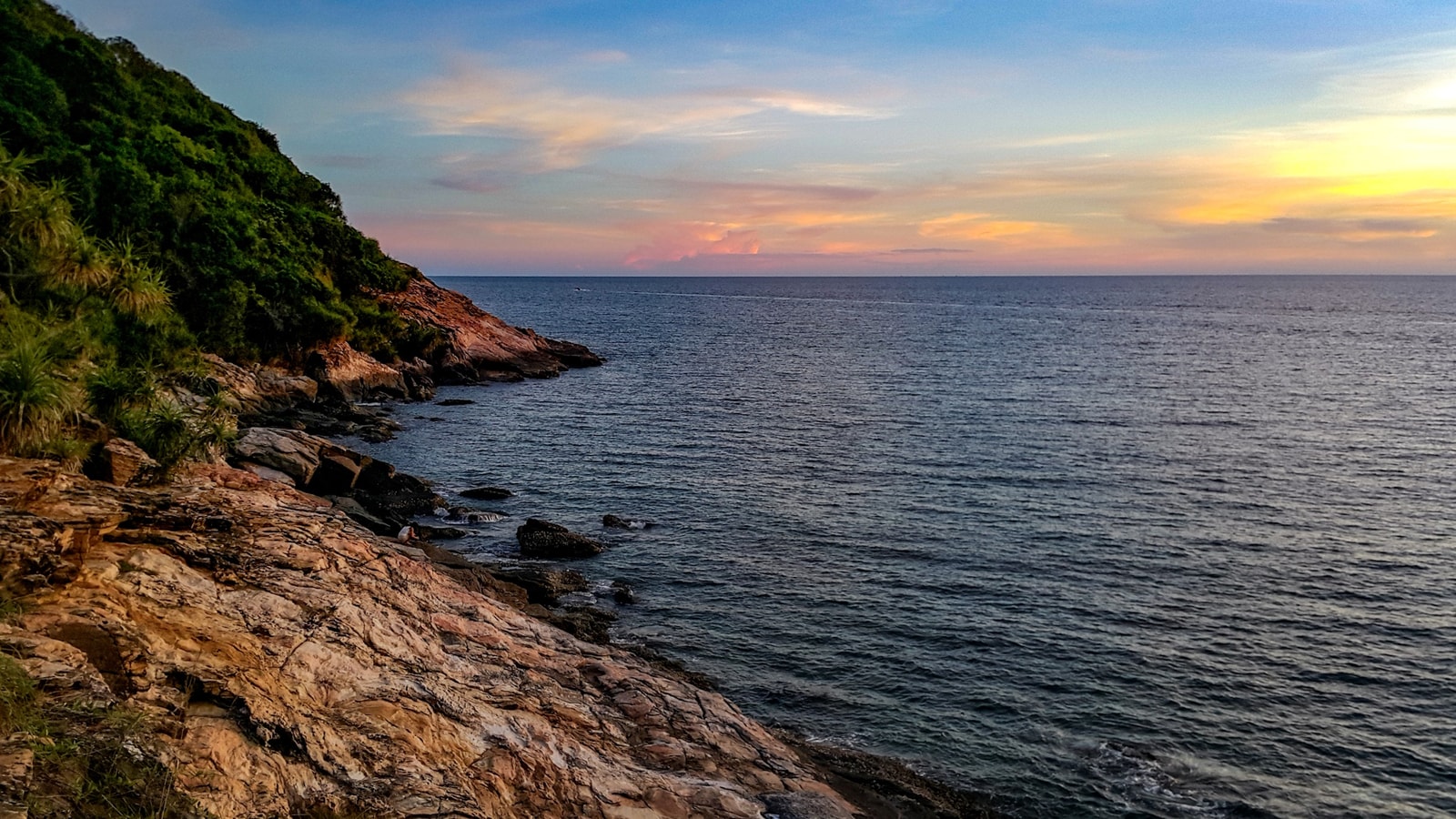 A dramatic sunset view over the water from Koh Samet, with the silhouette of a headland jutting into the sea.