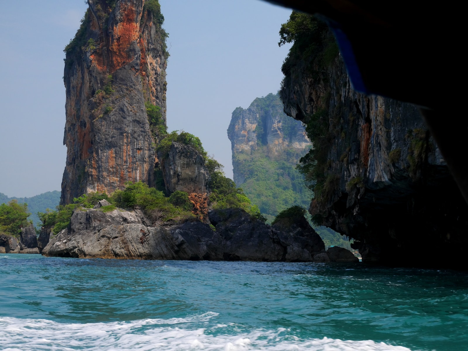 A view from a moving boat shows other boats navigating through the water towards towering, green-covered karst islands.