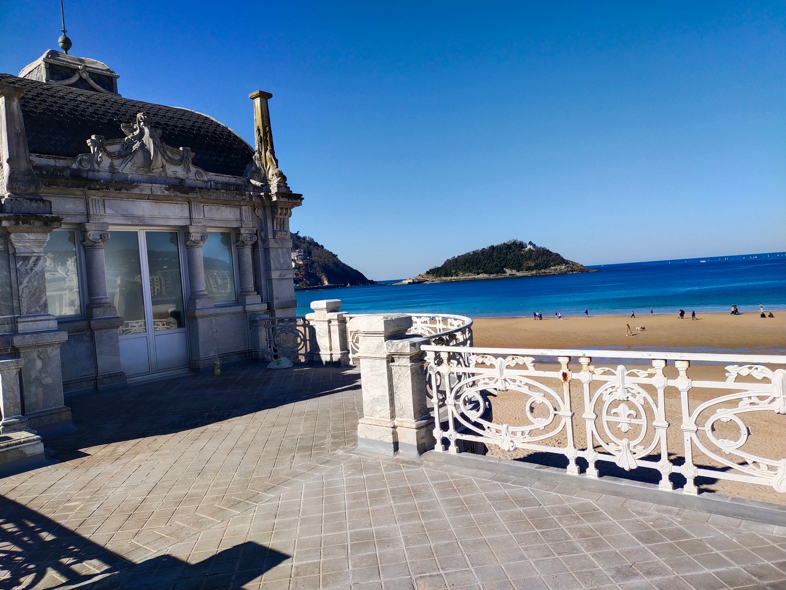 The ornate white railings of the promenade at La Concha beach, with a classical pavilion on the left and Santa Clara Island visible in the bay.