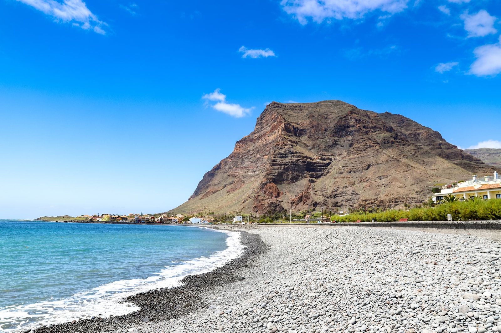 A curving turquoise bay at La Puntilla beach is framed by a massive volcanic mountain backdrop.