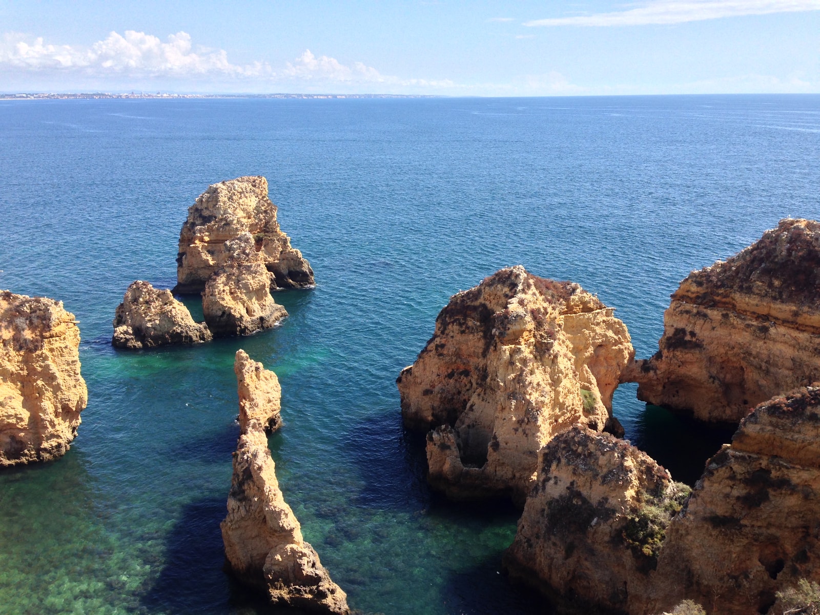 Golden limestone cliffs and sea stacks rise from turquoise water under a clear blue sky.