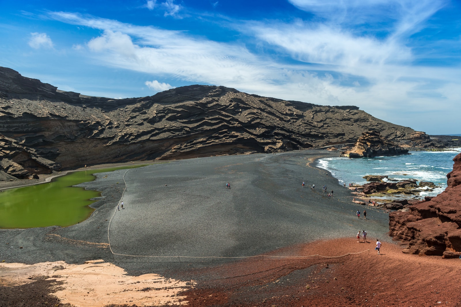 A bright turquoise lagoon is separated from the darker sea by a strip of black volcanic sand.