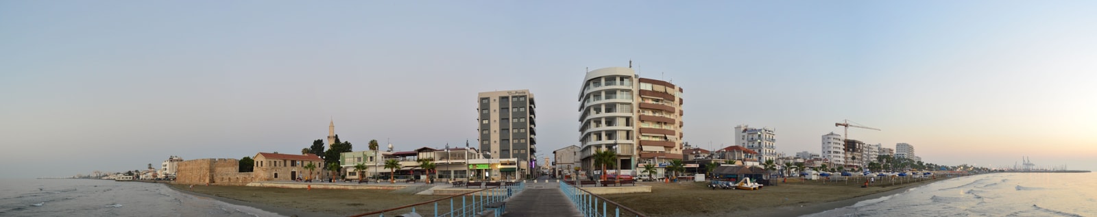 A panoramic view of Larnaca's seafront, showing the long stretch of beach, promenade, and the city.