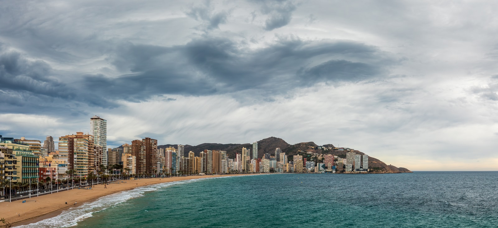 An elevated panoramic view of the wide, crescent-shaped Levante Beach bay in Benidorm, showcasing the dense city skyline.