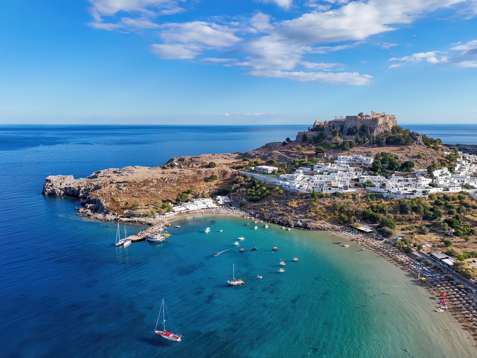 An aerial panorama of Lindos Bay shows the Acropolis on a promontory, the village, and the two main beaches within the bay.