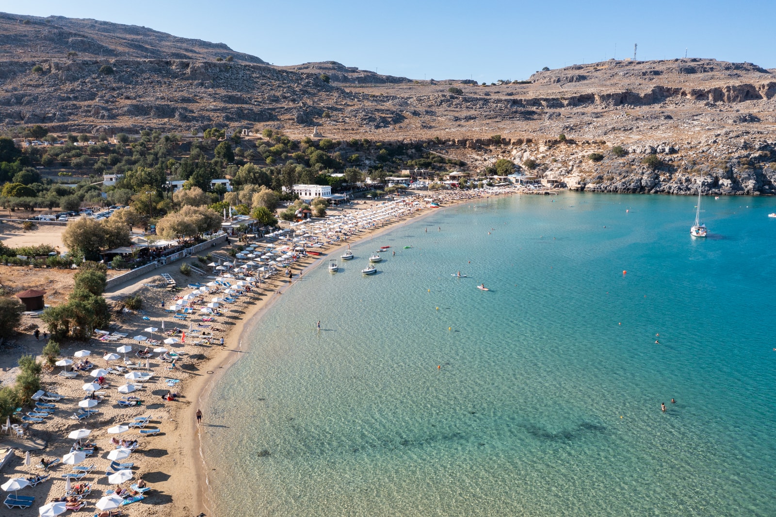 An aerial shot of Lindos Beach, showing rows of umbrellas and sunbeds on the golden sand next to turquoise water.