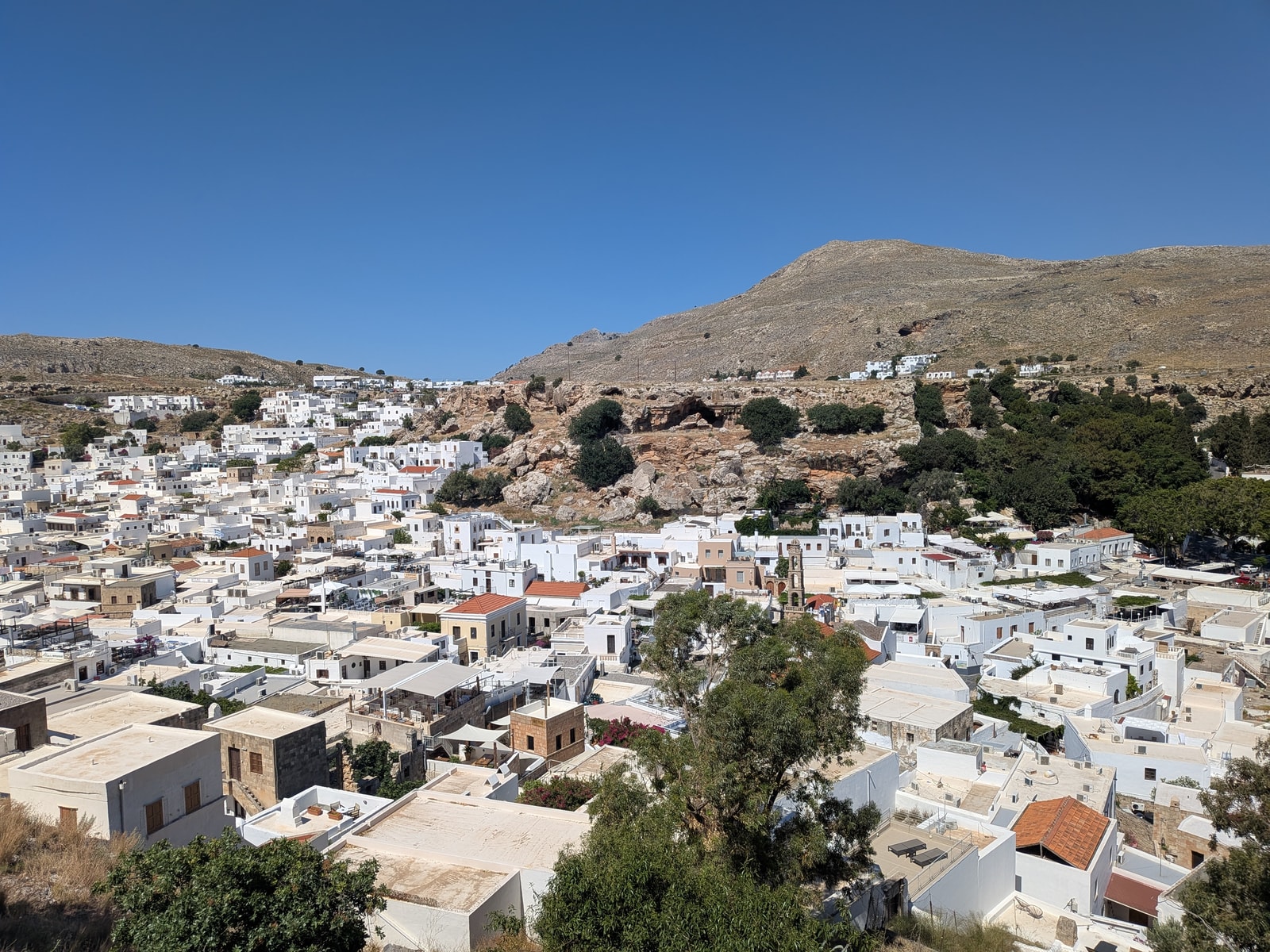 A view of the whitewashed village of Lindos nestled in a dry, hilly landscape.