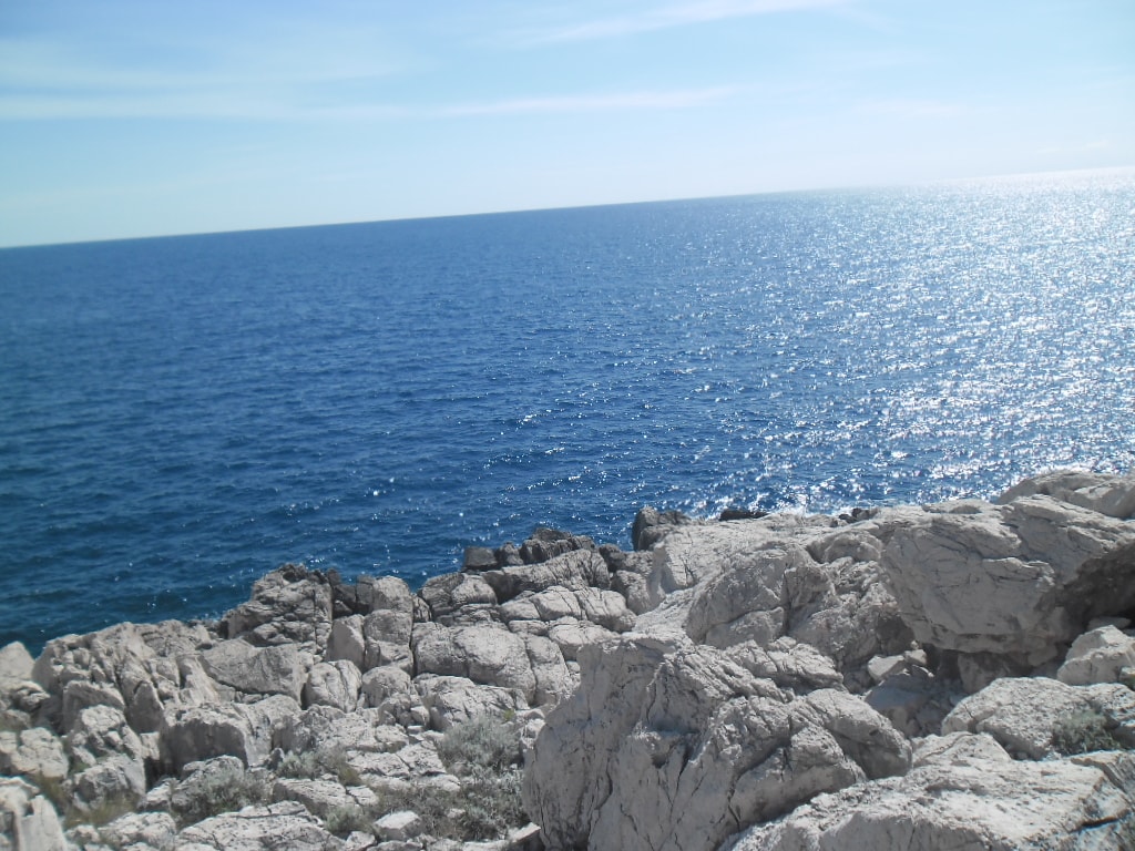 Exposed, layered rock formations on an island coast meet the deep blue Adriatic sea.