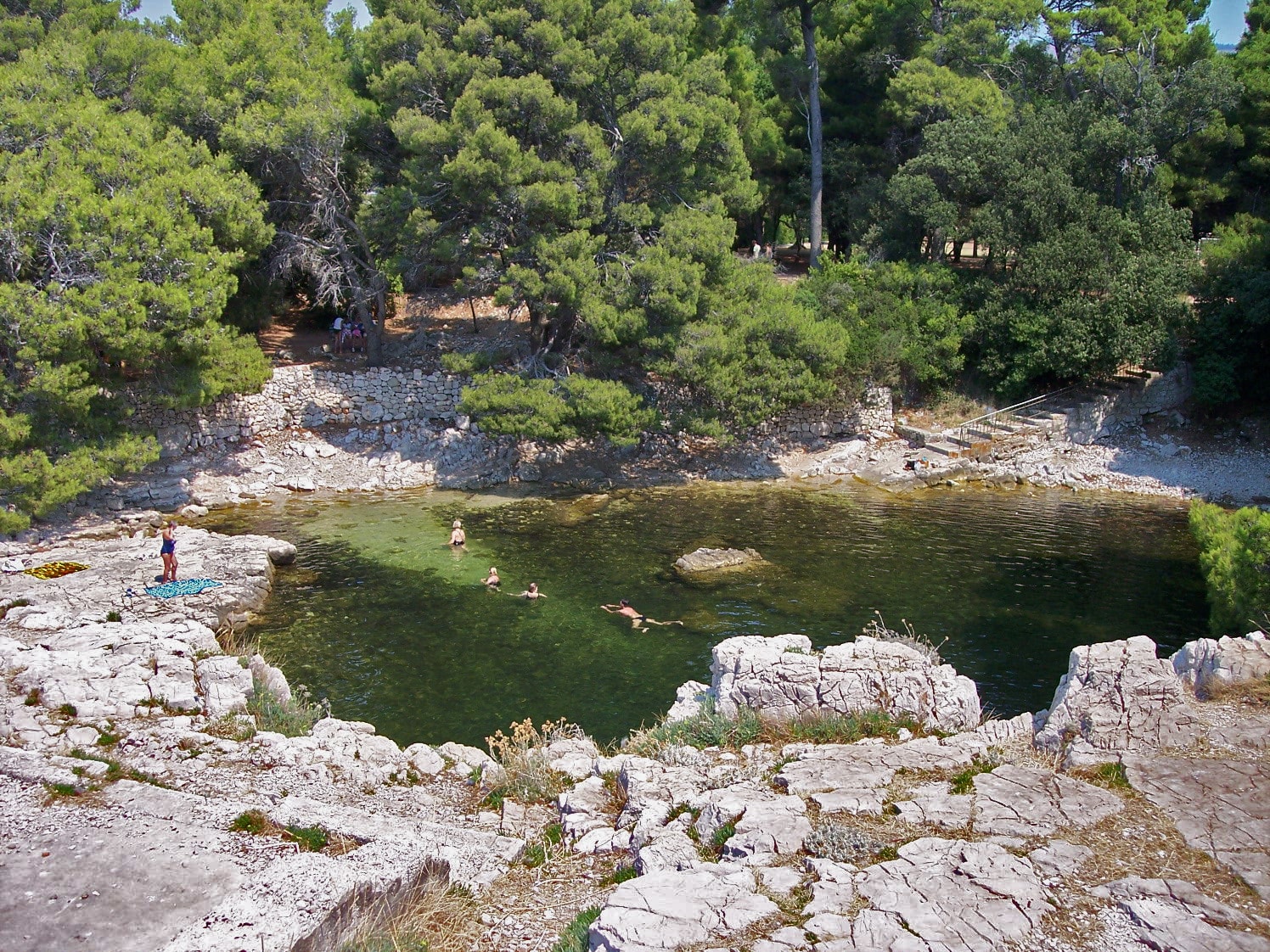 A small, sheltered rock pool on an island, with stone ledges and ladders for entering the clear water.