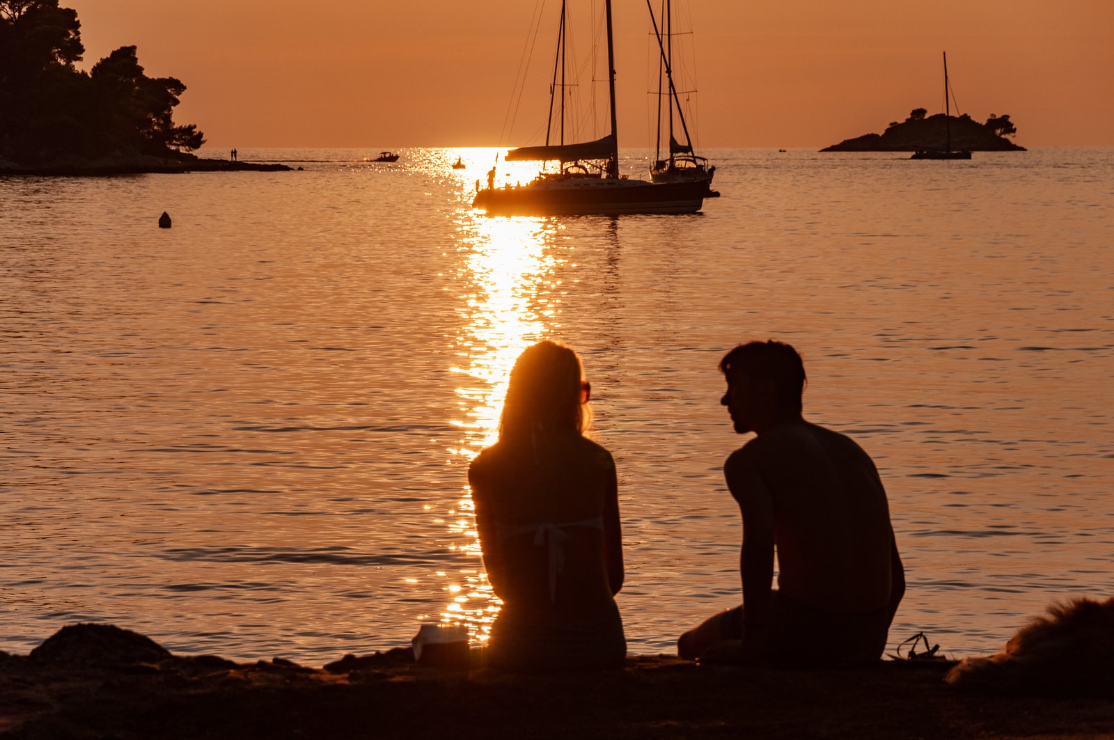 Silhouettes of two people on Lone Beach at dusk, with the warm golden sunset light shimmering across the water.