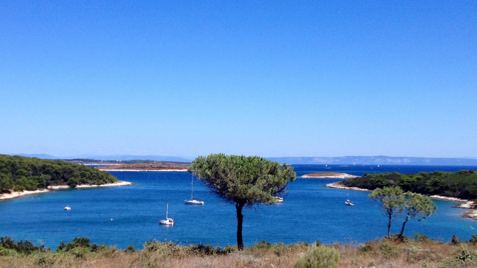 A view of Mali Portić, a rare sandy bay in Cape Kamenjak, with sailboats resting in its calm, sheltered waters.