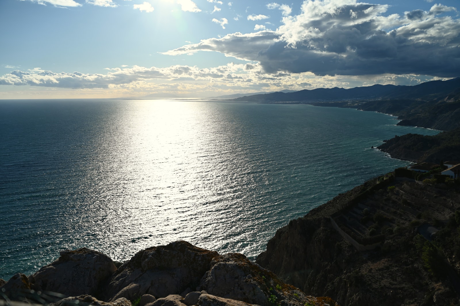 A broad, dramatic panorama of a protected coastline, with elevated cliffs, expansive blue sea, and distant headlands under atmospheric light.