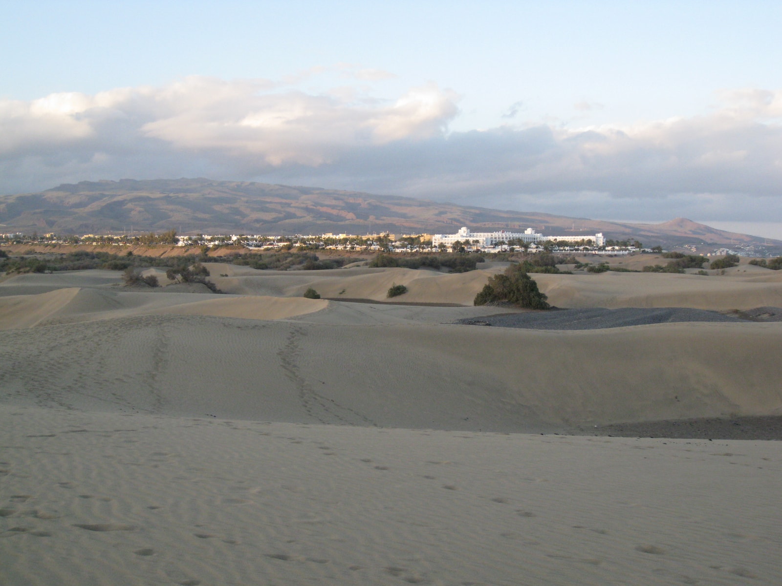 A large, modern hotel building stands right at the edge of the expansive Maspalomas sand dunes.