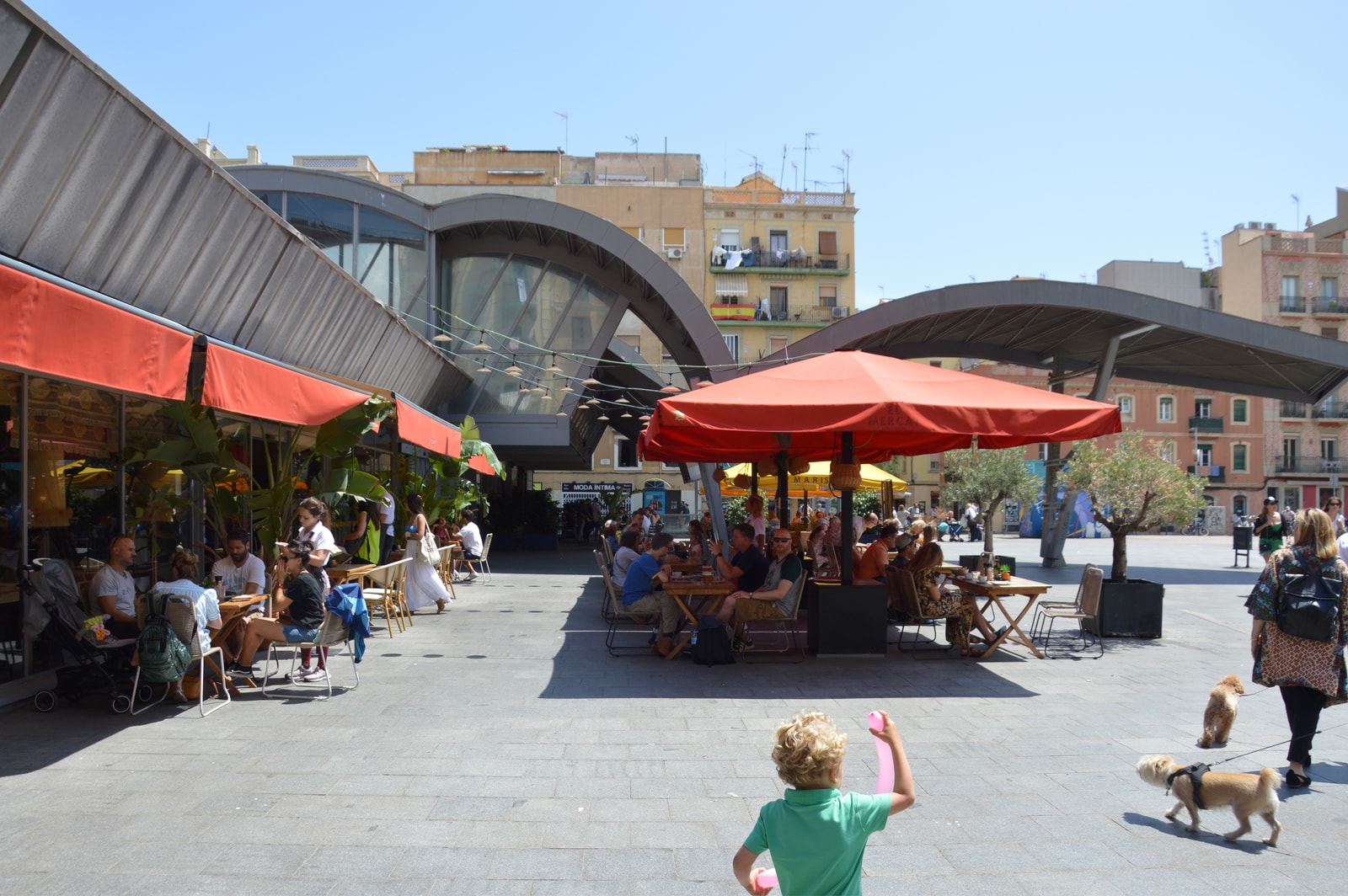 Diners sit at outdoor tables under umbrellas at a restaurant in the sunny Mercat de la Barceloneta.