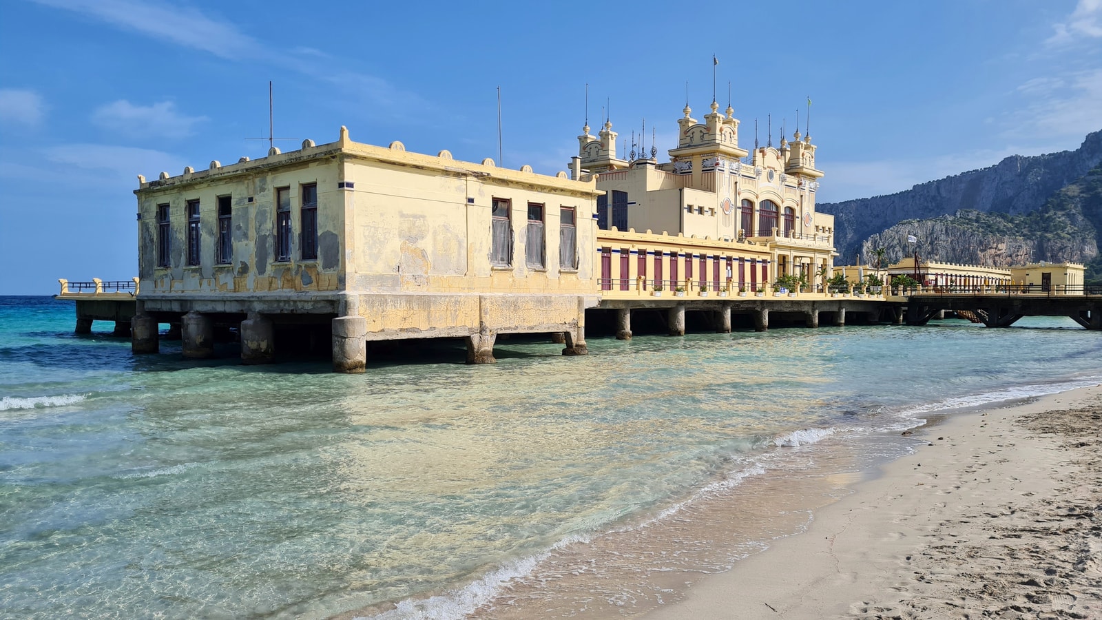 Side profile of the Antico Stabilimento Balneare, showing the reinforced concrete pylons that support it over the clear turquoise water.