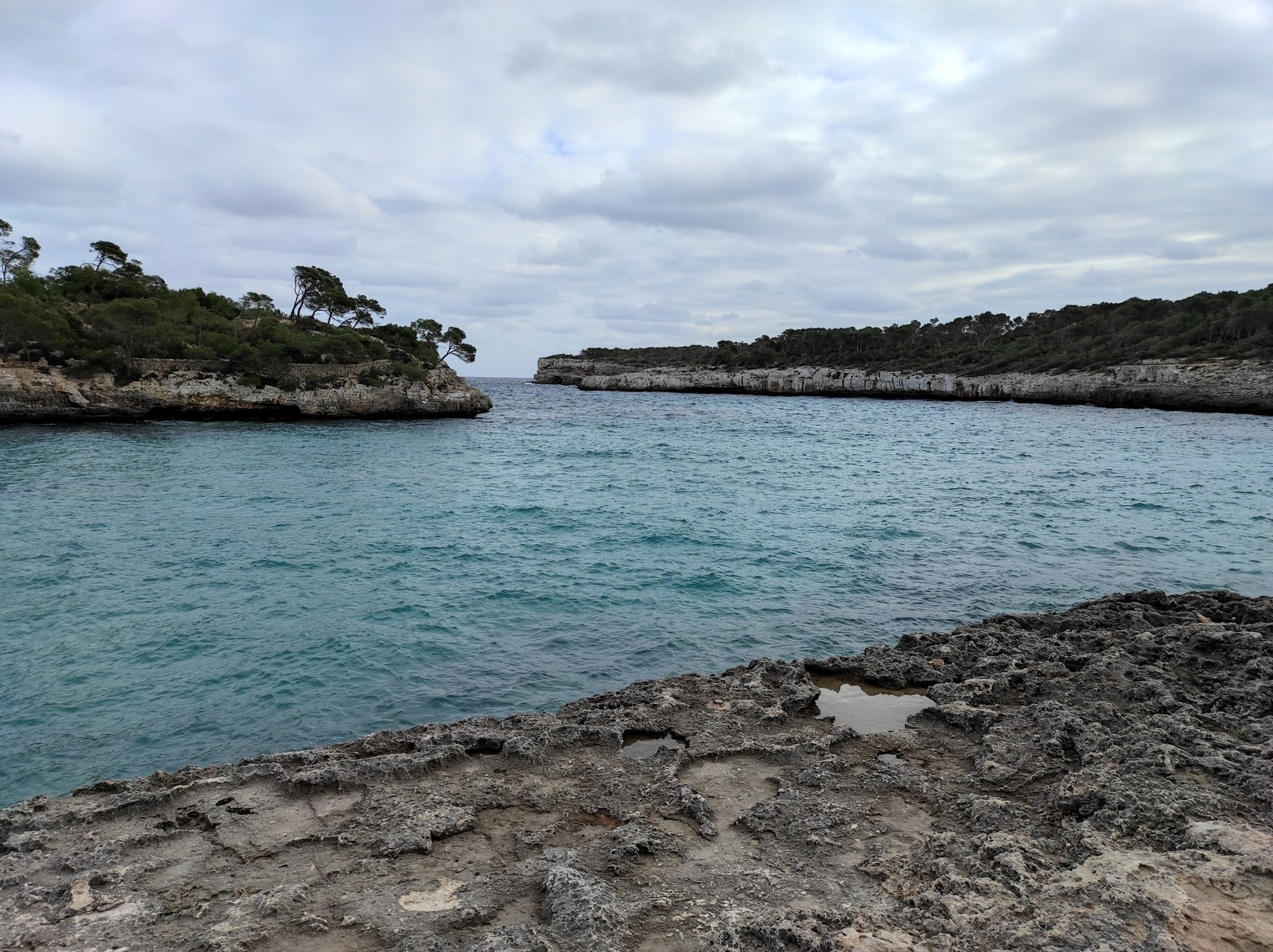 A scenic view of Mondragó Natural Park shows a turquoise inlet surrounded by layered limestone cliffs and Mediterranean vegetation.