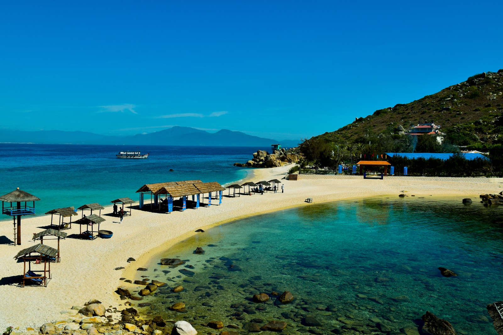 A stunning tropical lagoon with a strip of pale sand, clear shallow water, and lush green hills.