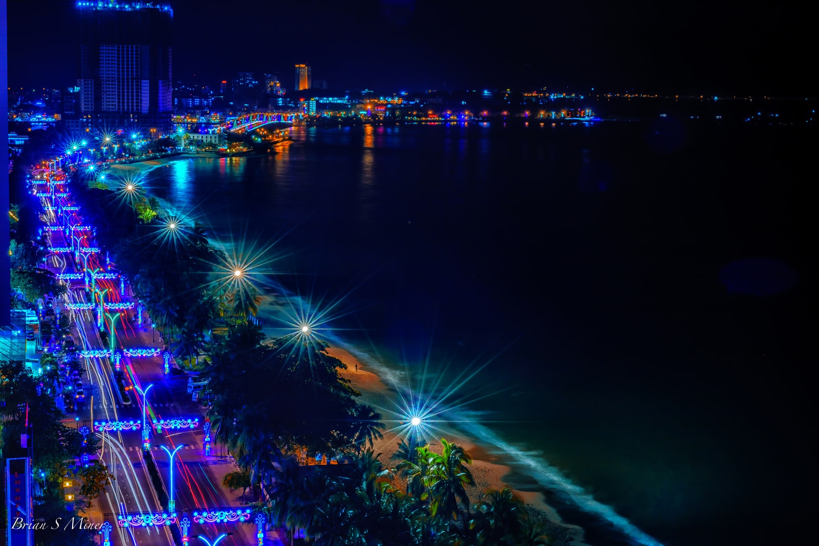 The illuminated beachfront of Nha Trang at night, showing the city skyline and coastal road.