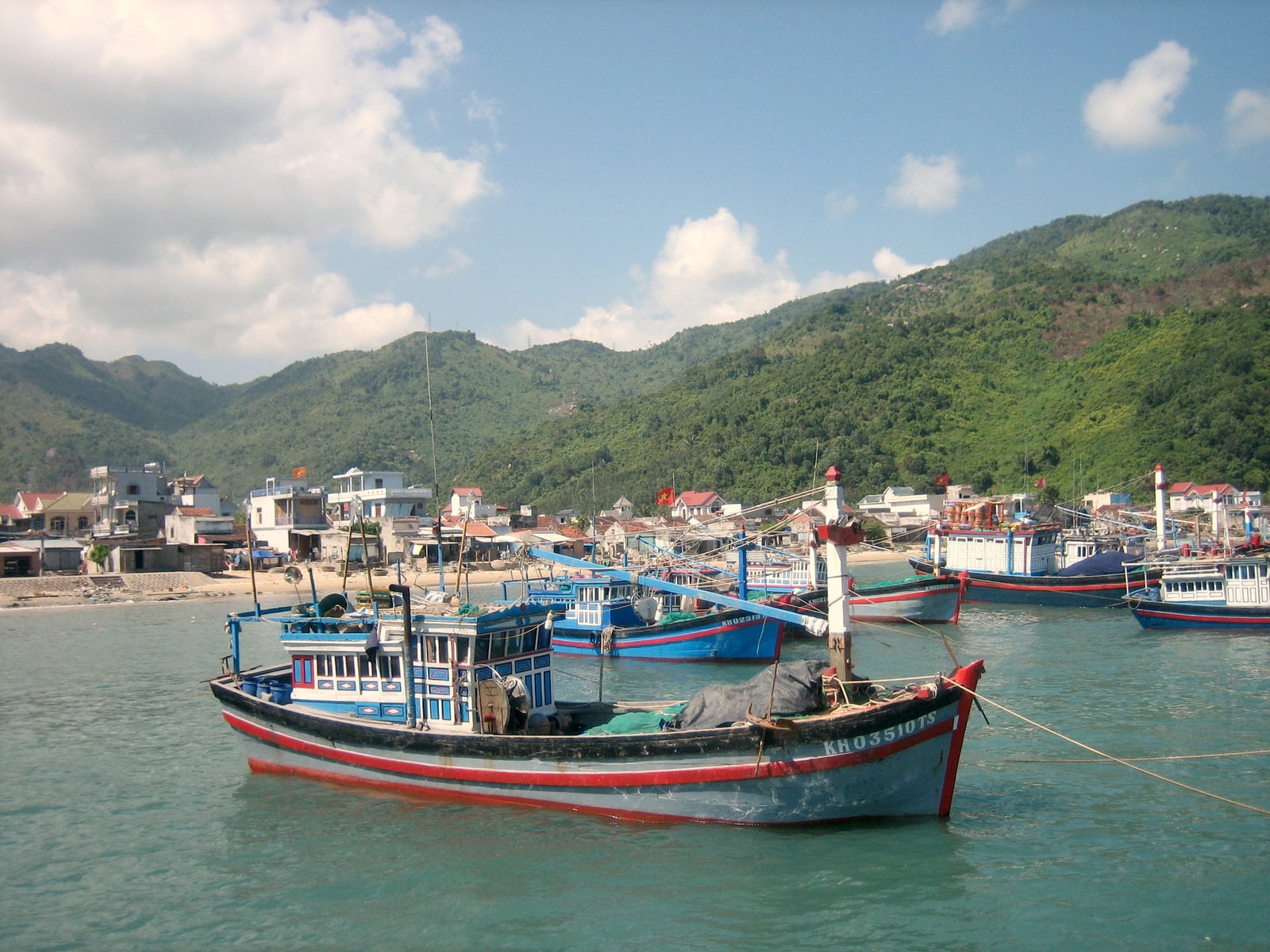 A vibrant fishing village scene with colorful boats moored in the harbor against a backdrop of coastal buildings.