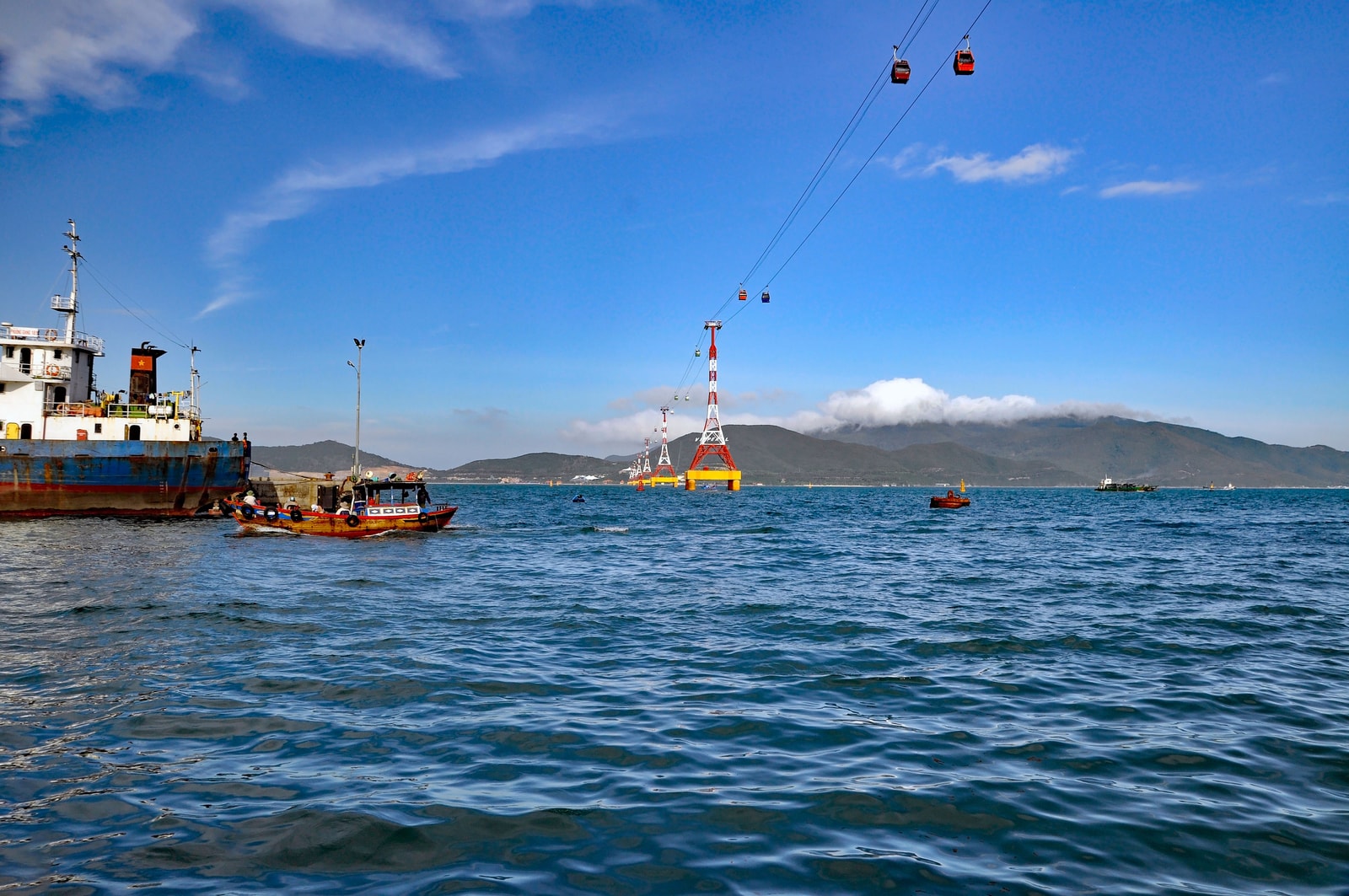 A cable car travels over the blue-green water of a bay, with mountainous islands in the background.