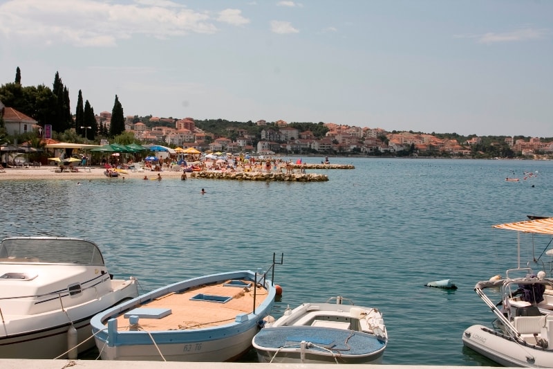Boats anchored in the bay with the bustling Okrug Gornji beach and its colorful umbrellas in the background.